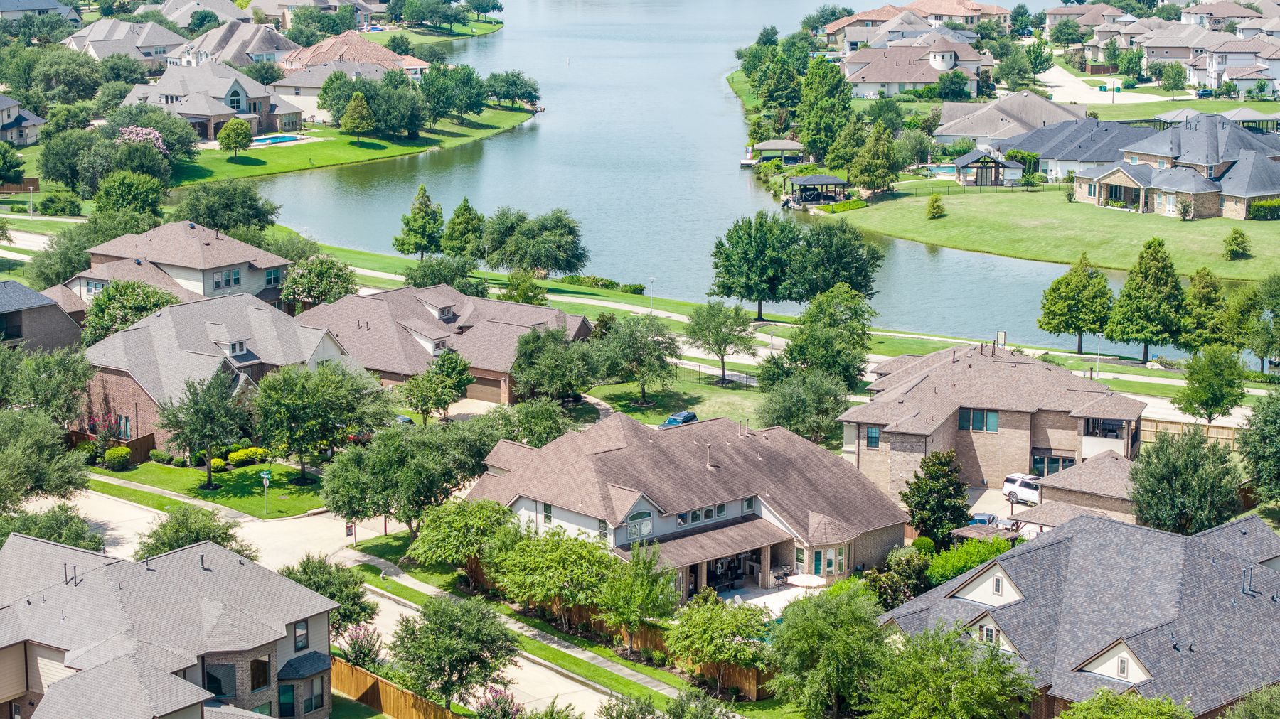Aerial of a lakeside neighborhood with a brick home in the foreground and a winding canal lined with trees