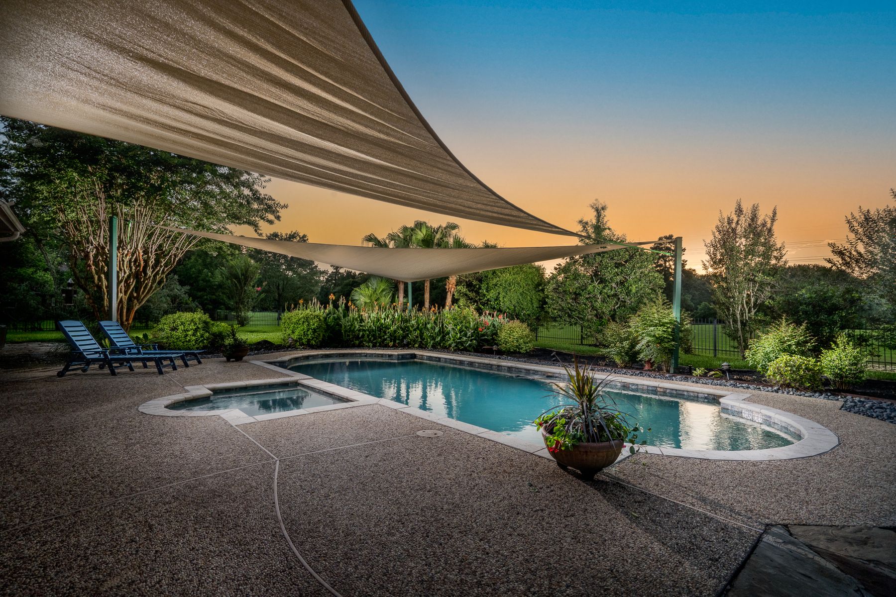 Twilight poolscape under two shade sails with a gradient sky from gold to deep blue