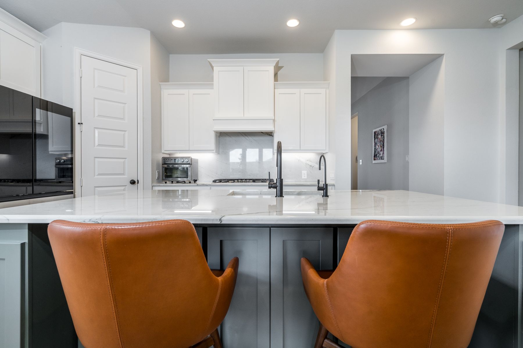 Kitchen island with white marble, charcoal cabinetry, and caramel leather counter stools facing a white range hood